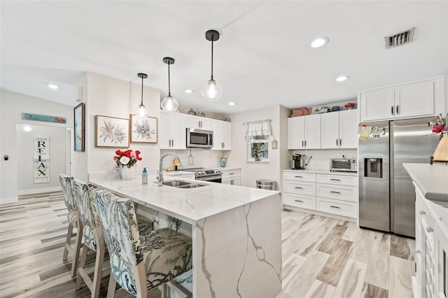 kitchen featuring appliances with stainless steel finishes, backsplash, light wood-type flooring, white cabinets, and hanging light fixtures