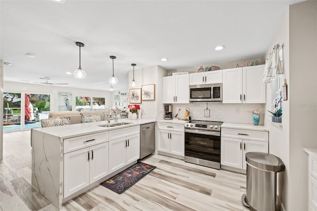 kitchen featuring appliances with stainless steel finishes, light hardwood / wood-style flooring, sink, kitchen peninsula, and ceiling fan