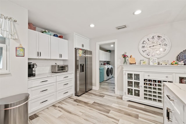 kitchen featuring light stone counters, light hardwood / wood-style floors, stainless steel refrigerator with ice dispenser, tasteful backsplash, and washer and clothes dryer