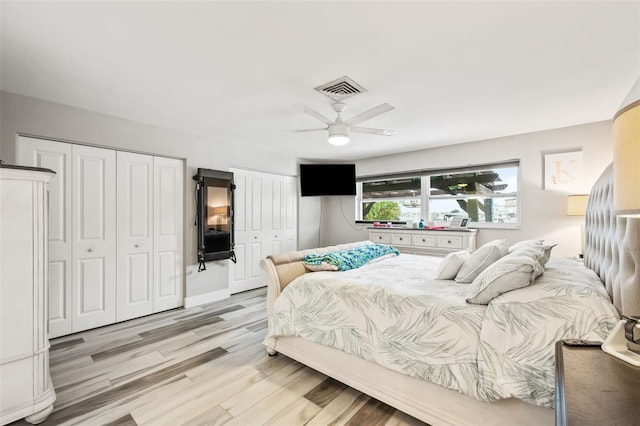 bedroom featuring light wood finished floors, visible vents, a ceiling fan, and multiple closets