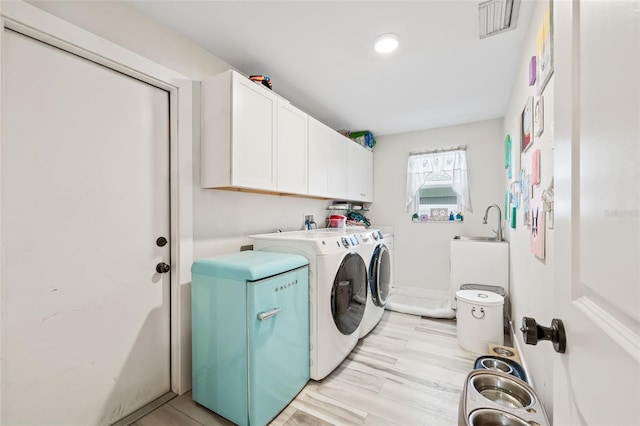clothes washing area featuring light wood finished floors, visible vents, separate washer and dryer, cabinet space, and a sink