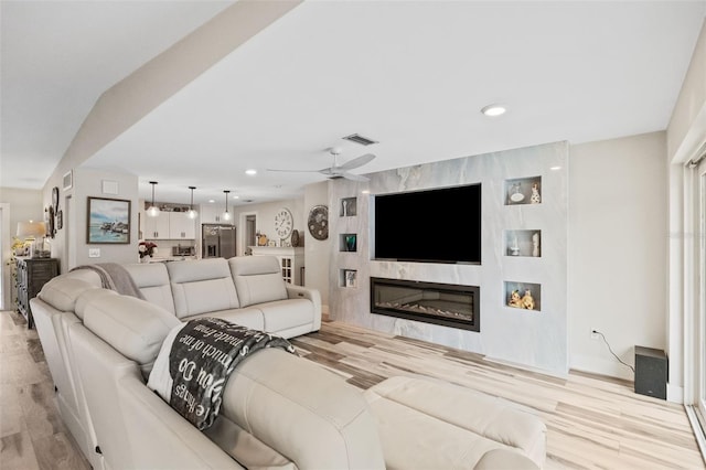 living room featuring light hardwood / wood-style flooring, ceiling fan, and a large fireplace