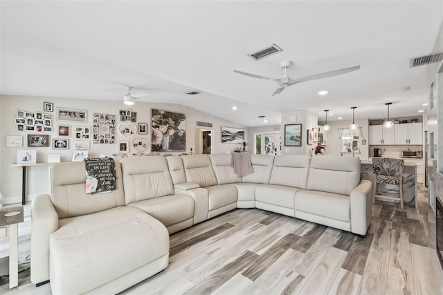 living room with light wood finished floors, visible vents, a ceiling fan, and vaulted ceiling