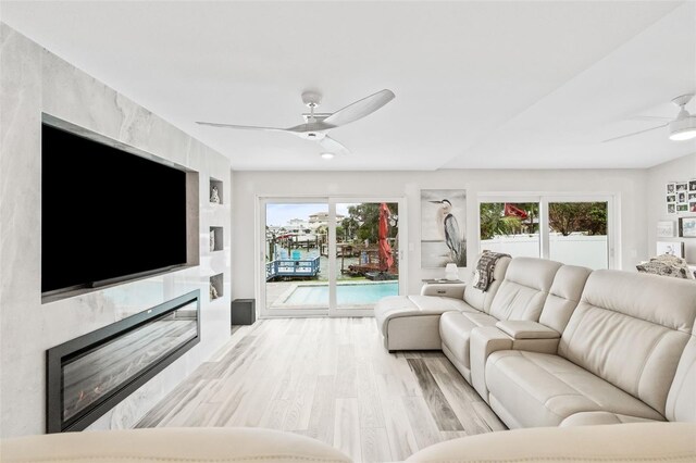 living room with light wood finished floors, a ceiling fan, and a high end fireplace