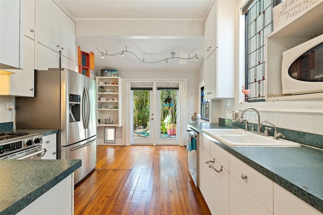 kitchen featuring light wood finished floors, tasteful backsplash, appliances with stainless steel finishes, white cabinetry, and a sink