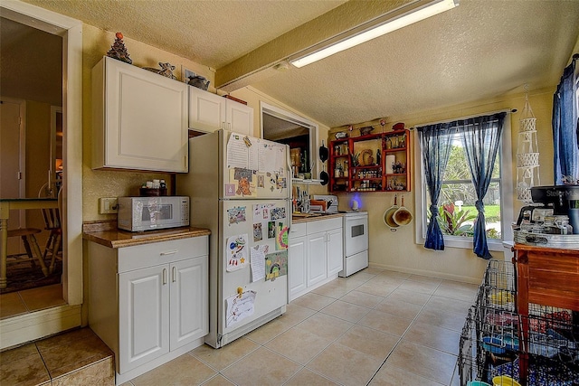 kitchen with light tile patterned floors, white appliances, a textured ceiling, and white cabinets