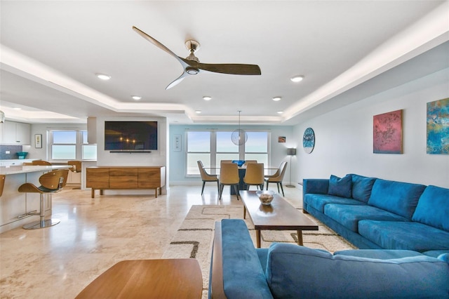 tiled living room with a tray ceiling and ceiling fan