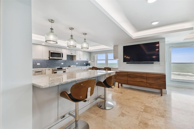 kitchen with a breakfast bar area, appliances with stainless steel finishes, white cabinetry, a tray ceiling, and decorative light fixtures