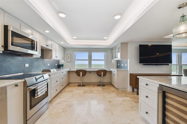 kitchen with a raised ceiling, wine cooler, appliances with stainless steel finishes, backsplash, and light tile patterned floors