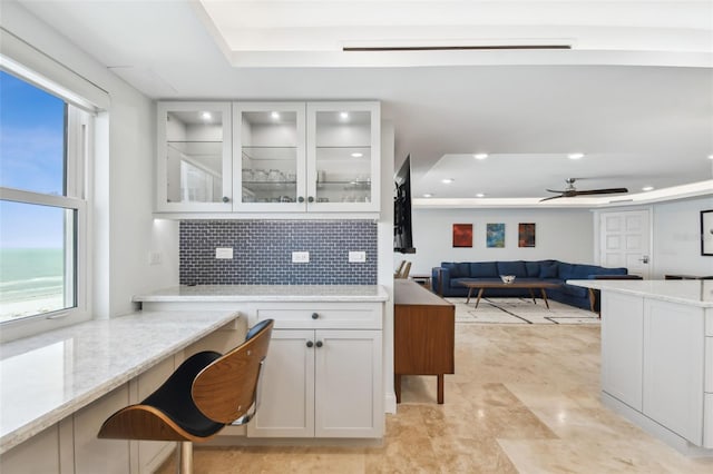 interior space with tasteful backsplash, a raised ceiling, white cabinets, and ceiling fan