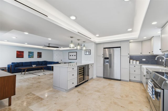 kitchen featuring kitchen peninsula, wine cooler, premium appliances, a tray ceiling, and tasteful backsplash