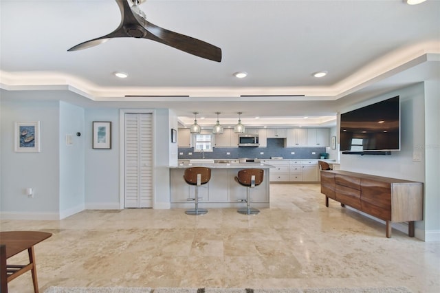 kitchen featuring tasteful backsplash, a breakfast bar area, a raised ceiling, light tile patterned floors, and ceiling fan