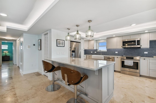 kitchen featuring decorative backsplash, appliances with stainless steel finishes, a raised ceiling, and light stone counters