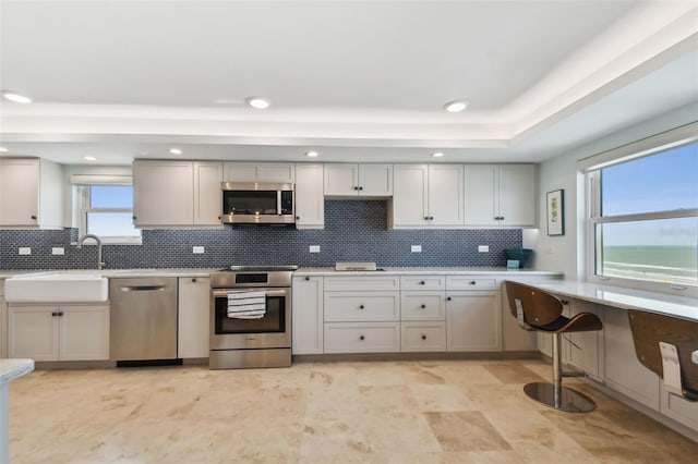 kitchen with backsplash, a tray ceiling, stainless steel appliances, and light tile patterned flooring