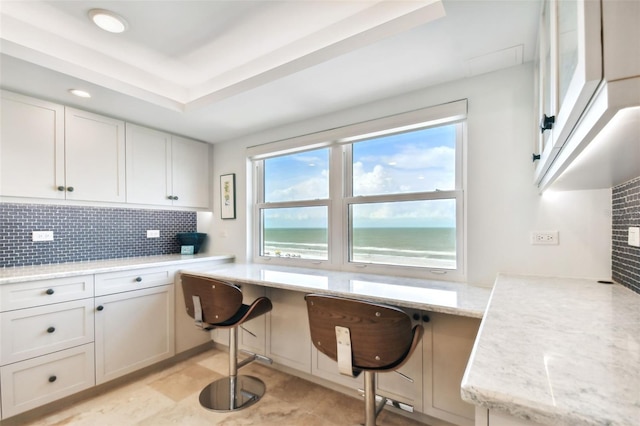 kitchen featuring light tile patterned floors, a breakfast bar, tasteful backsplash, white cabinetry, and light stone counters