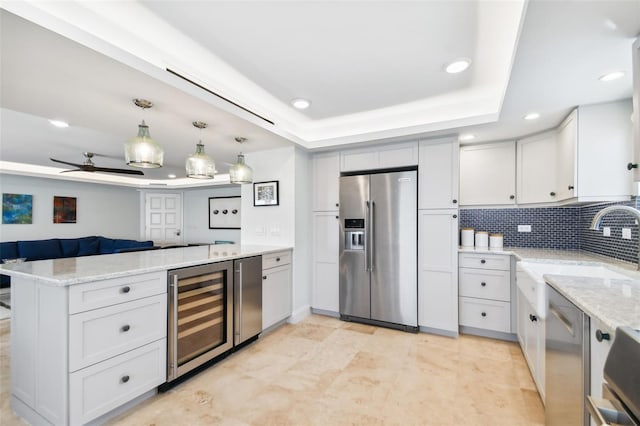 kitchen with tasteful backsplash, a raised ceiling, stainless steel appliances, beverage cooler, and kitchen peninsula