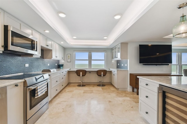 5000 Gulf Blvd Unit 704, St Pete Beach, FL 33706 - kitchen with beverage cooler, stainless steel appliances, decorative backsplash, glass insert cabinets, and a tray ceiling