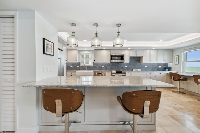 5000 Gulf Blvd Unit 704, St Pete Beach, FL 33706 - kitchen with stainless steel appliances, a tray ceiling, a peninsula, a kitchen breakfast bar, and tasteful backsplash