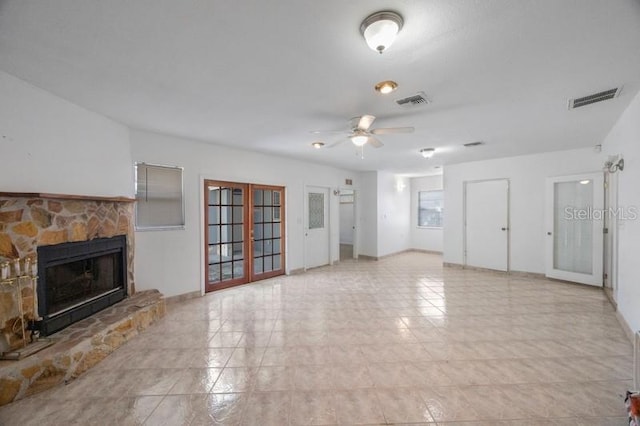 unfurnished living room featuring french doors, ceiling fan, light tile patterned flooring, and a stone fireplace