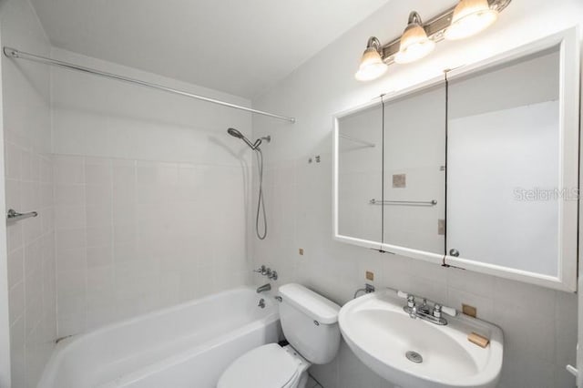 full bathroom featuring toilet, sink, tile walls, tiled shower / bath combo, and tasteful backsplash