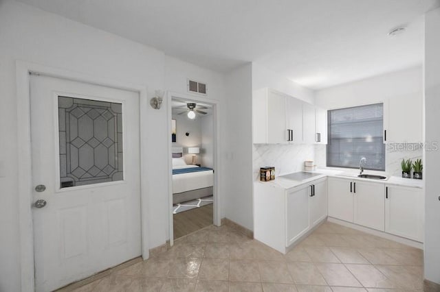 kitchen with light tile patterned floors, tasteful backsplash, sink, ceiling fan, and white cabinets