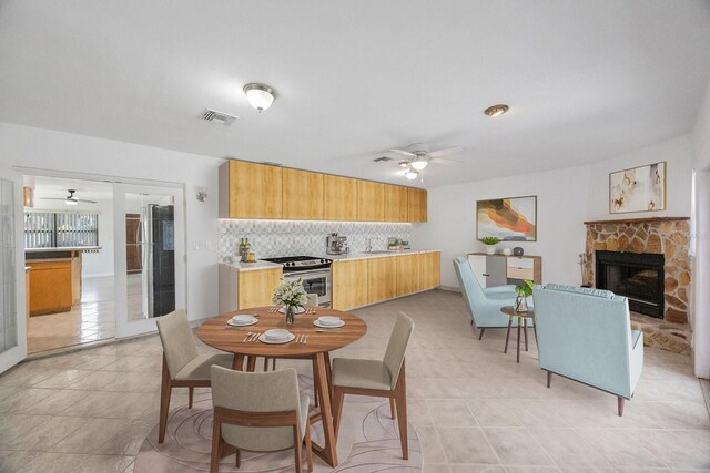 tiled dining area with ceiling fan and a stone fireplace