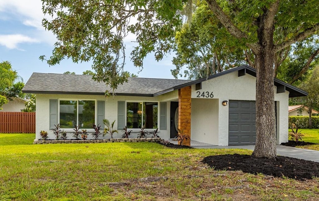 view of front facade featuring stucco siding, a shingled roof, fence, a garage, and a front lawn