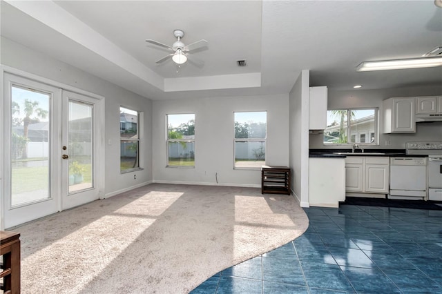 unfurnished living room featuring french doors, a tray ceiling, ceiling fan, sink, and dark colored carpet