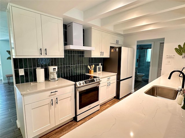 kitchen with tasteful backsplash, stainless steel electric range oven, freestanding refrigerator, a sink, and wall chimney exhaust hood