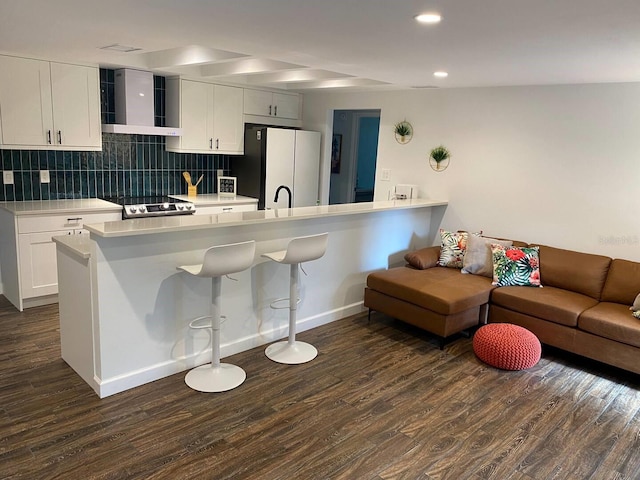 kitchen featuring freestanding refrigerator, light countertops, wall chimney range hood, a kitchen bar, and dark wood-style floors