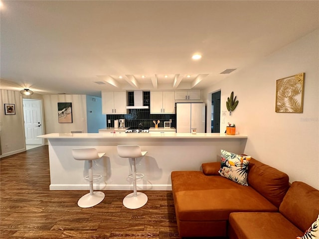 kitchen featuring wall chimney range hood, visible vents, light countertops, freestanding refrigerator, and dark wood finished floors