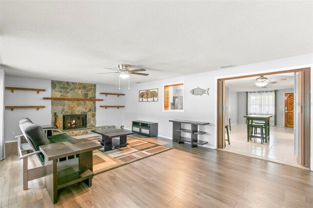 living room with a fireplace, light hardwood / wood-style flooring, ceiling fan, and a textured ceiling