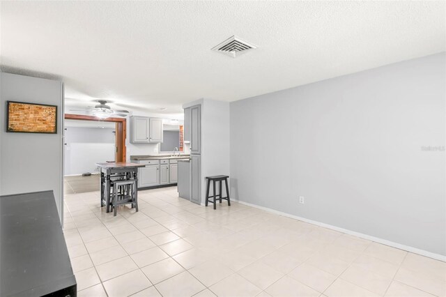 interior space with ceiling fan, sink, light tile patterned flooring, and a textured ceiling