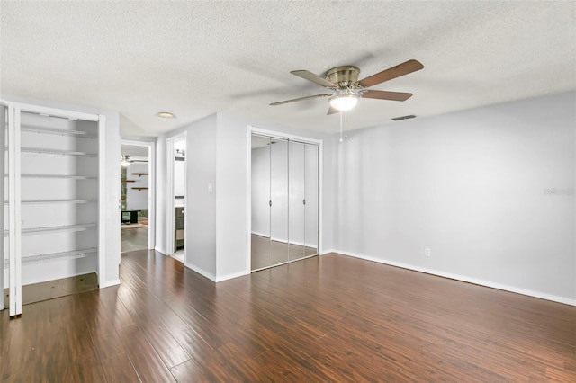 unfurnished bedroom featuring a textured ceiling, ceiling fan, hardwood / wood-style floors, and two closets