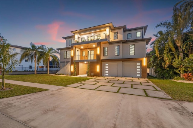 view of front of home with concrete driveway, a lawn, a balcony, stairs, and stucco siding