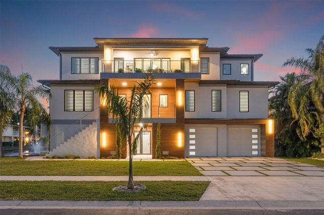 contemporary house with a front yard, driveway, a balcony, and stucco siding