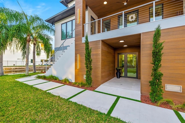 entrance to property with a balcony, ceiling fan, and a lawn