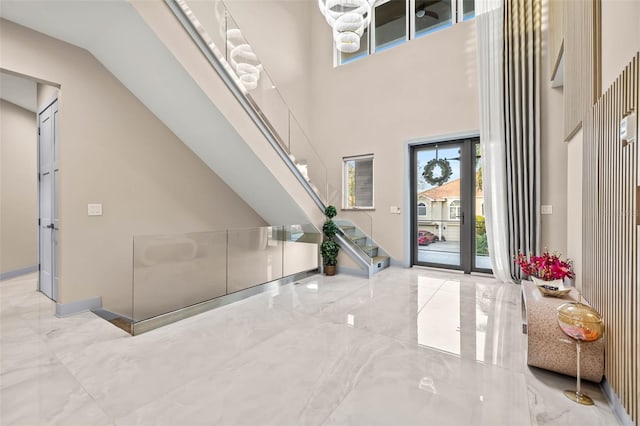 foyer entrance featuring marble finish floor, a towering ceiling, baseboards, and stairs