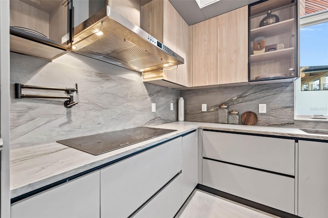 kitchen with black electric cooktop, wall chimney range hood, light brown cabinetry, tasteful backsplash, and modern cabinets