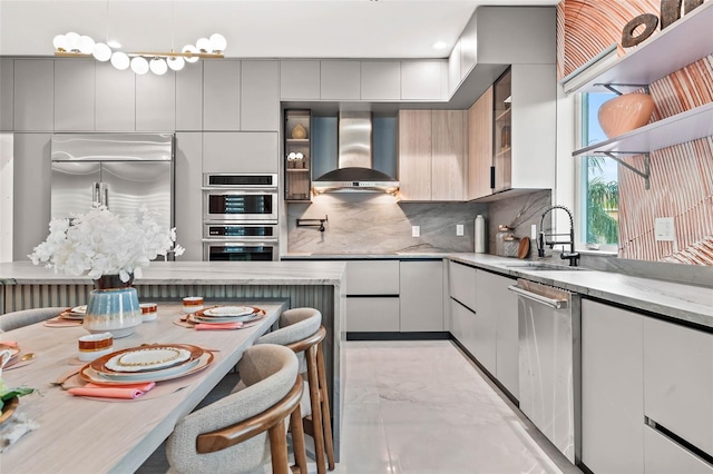 kitchen featuring tasteful backsplash, modern cabinets, appliances with stainless steel finishes, wall chimney range hood, and a sink