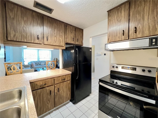 kitchen featuring stainless steel electric range oven, exhaust hood, light tile patterned floors, a textured ceiling, and black refrigerator