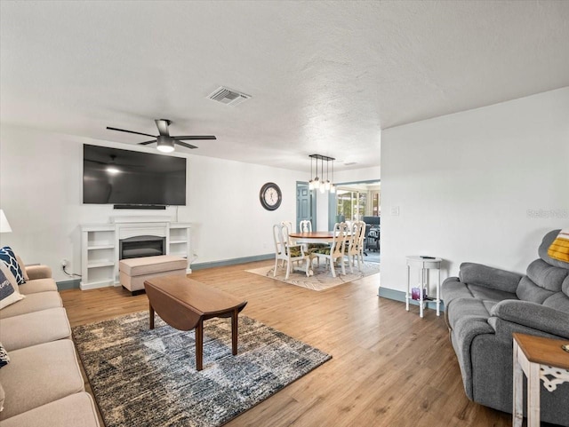 living room with light hardwood / wood-style floors, ceiling fan with notable chandelier, and a textured ceiling