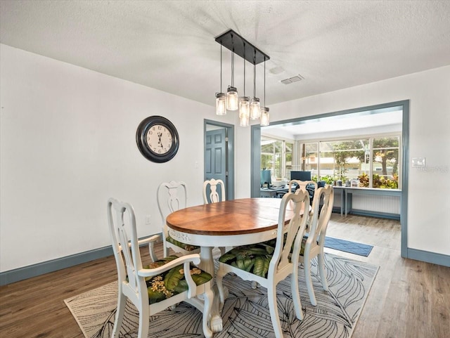 dining area with a notable chandelier, light hardwood / wood-style flooring, and a textured ceiling