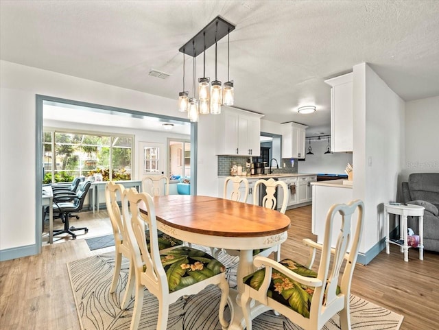 dining room with sink, a notable chandelier, light hardwood / wood-style floors, and a textured ceiling