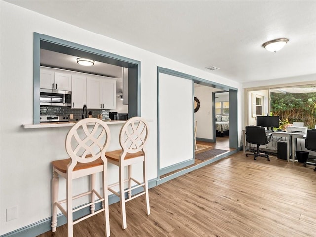 kitchen with white cabinetry, decorative backsplash, a kitchen breakfast bar, and light wood-type flooring