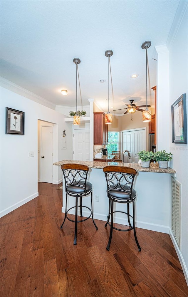 kitchen with decorative light fixtures, ornamental molding, ceiling fan, kitchen peninsula, and dark wood-type flooring