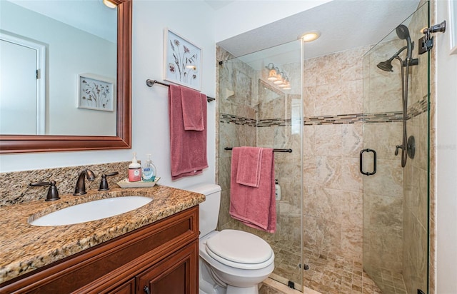 bathroom featuring a shower with shower door, toilet, and vanity