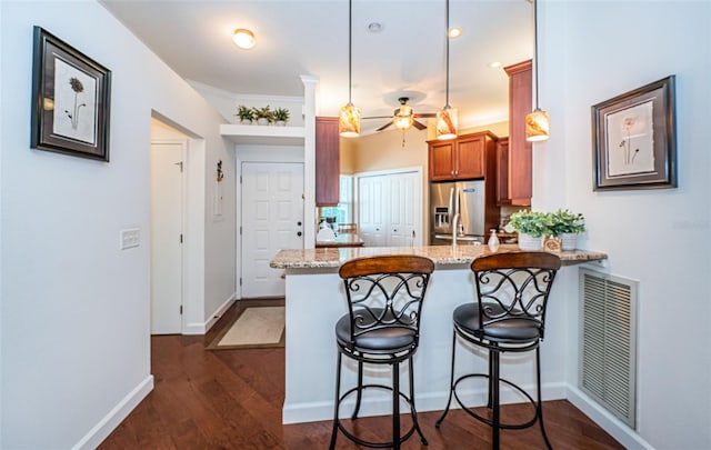 kitchen featuring stainless steel fridge with ice dispenser, dark wood-type flooring, a breakfast bar, decorative light fixtures, and kitchen peninsula