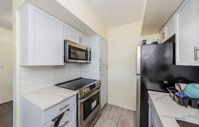 kitchen featuring white cabinets, light wood-type flooring, backsplash, and stainless steel appliances