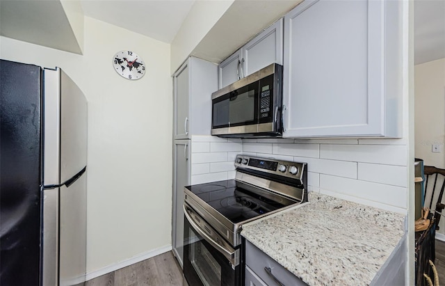 kitchen with stainless steel appliances, light stone countertops, decorative backsplash, and light hardwood / wood-style flooring